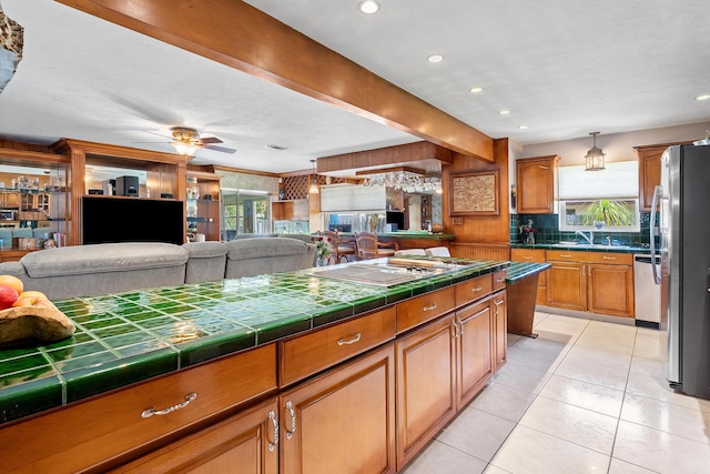 kitchen featuring stainless steel appliances, brown cabinets, open floor plan, tile counters, and decorative backsplash