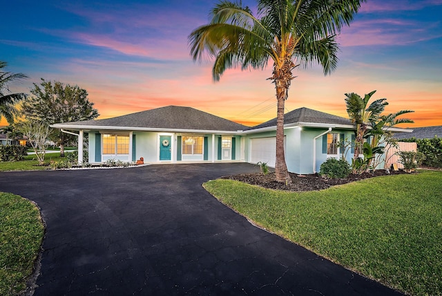 single story home with an attached garage, a front lawn, aphalt driveway, and stucco siding