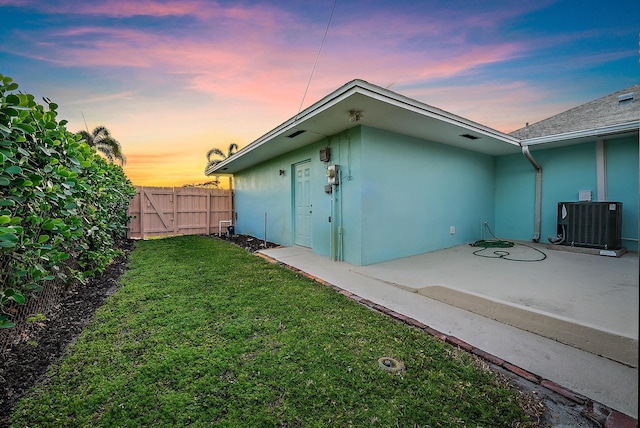 back of property at dusk featuring a yard, central AC unit, fence, and stucco siding