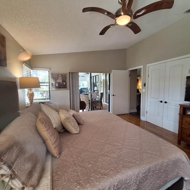 bedroom with ceiling fan, vaulted ceiling, a textured ceiling, and wood finished floors