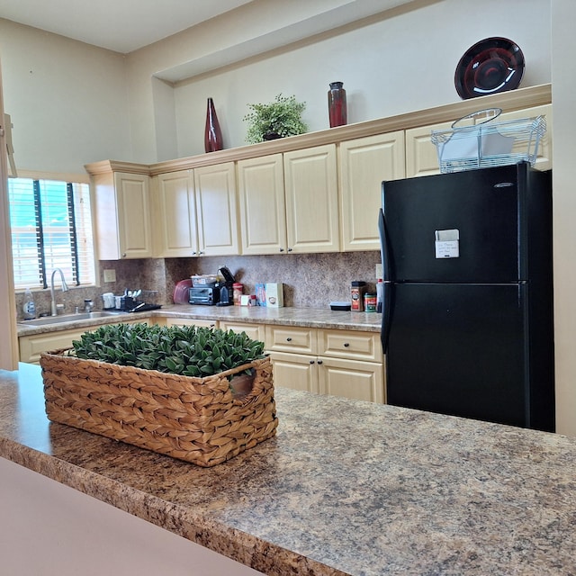kitchen with cream cabinetry, backsplash, a sink, and freestanding refrigerator