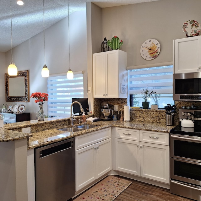 kitchen with appliances with stainless steel finishes, white cabinets, vaulted ceiling, a sink, and a peninsula