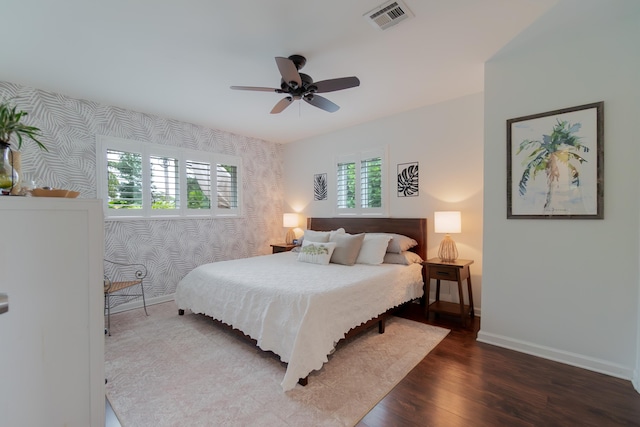 bedroom with wallpapered walls, baseboards, visible vents, and wood finished floors