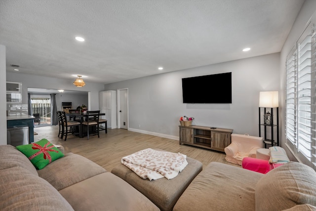 living area with recessed lighting, light wood-style flooring, baseboards, and a textured ceiling