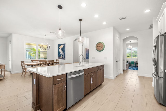 kitchen featuring arched walkways, an inviting chandelier, a kitchen island with sink, stainless steel appliances, and a sink