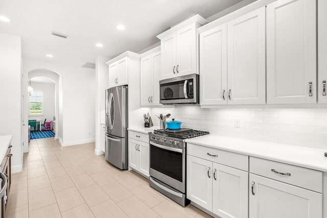 kitchen with appliances with stainless steel finishes, arched walkways, light countertops, and backsplash