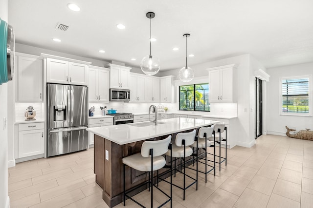 kitchen featuring stainless steel appliances, a sink, white cabinetry, light countertops, and a kitchen bar