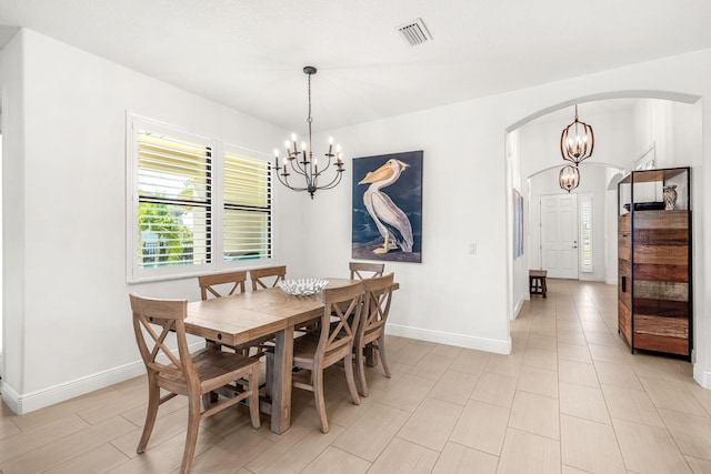 dining space with an inviting chandelier, visible vents, arched walkways, and baseboards