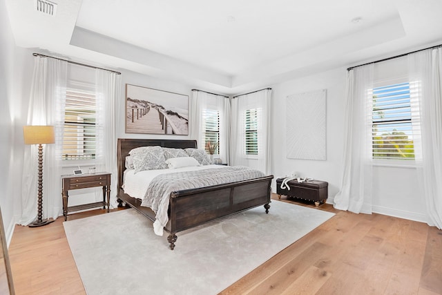 bedroom with light wood-style flooring, a raised ceiling, visible vents, and baseboards