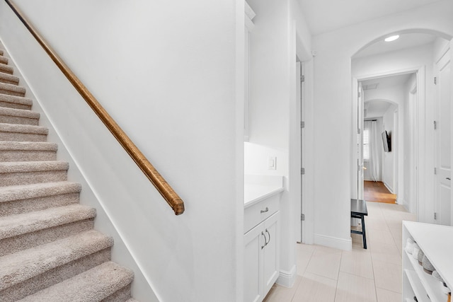 stairs featuring baseboards, arched walkways, and tile patterned floors