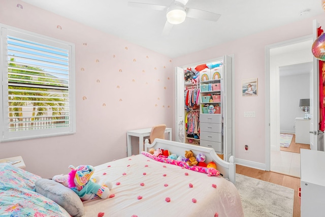 bedroom featuring baseboards, ceiling fan, a walk in closet, light wood-type flooring, and a closet