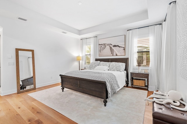 bedroom with baseboards, a tray ceiling, visible vents, and light wood-style floors