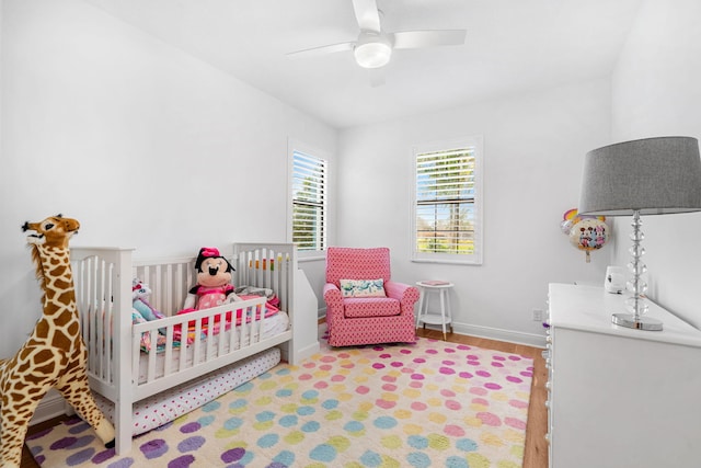 bedroom with a crib, ceiling fan, baseboards, and wood finished floors