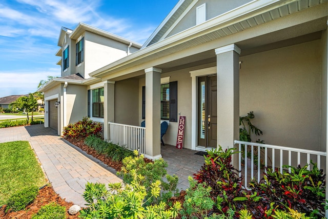 view of exterior entry with covered porch, decorative driveway, and stucco siding