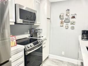 kitchen featuring appliances with stainless steel finishes, light countertops, baseboards, and white cabinetry