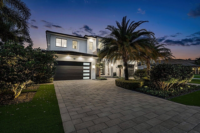 view of front of home with decorative driveway, an attached garage, and stucco siding