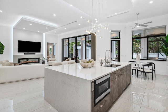 kitchen with stainless steel microwave, a glass covered fireplace, open floor plan, a sink, and an island with sink