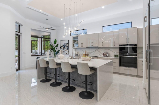 kitchen featuring an island with sink, modern cabinets, a high ceiling, and hanging light fixtures