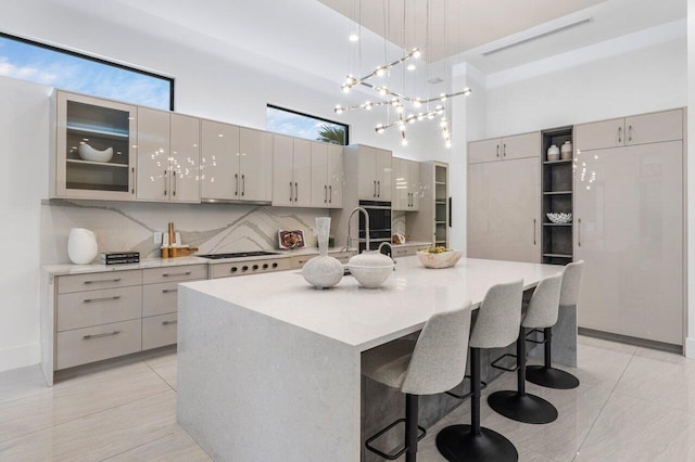 kitchen featuring white gas stovetop, a high ceiling, light countertops, an island with sink, and glass insert cabinets