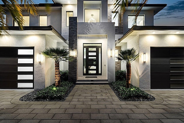 exterior entry at dusk featuring a garage and stucco siding