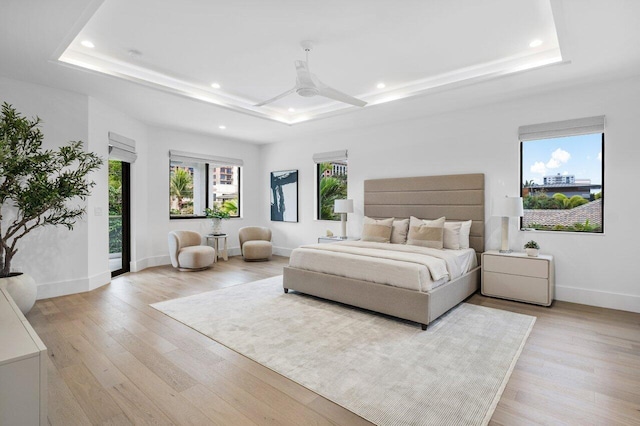 bedroom with a tray ceiling, multiple windows, and light wood-style flooring