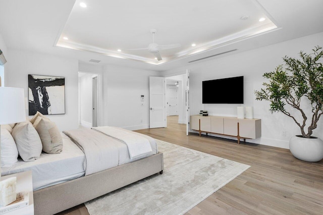 bedroom with light wood-style flooring and a tray ceiling