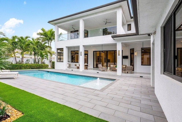 back of property featuring ceiling fan, a balcony, stucco siding, an outdoor pool, and a patio area