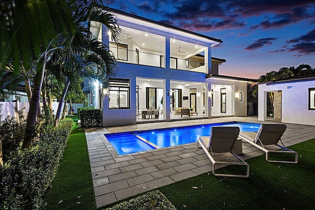 back of house at dusk with a pool with connected hot tub, a patio, a balcony, and stucco siding