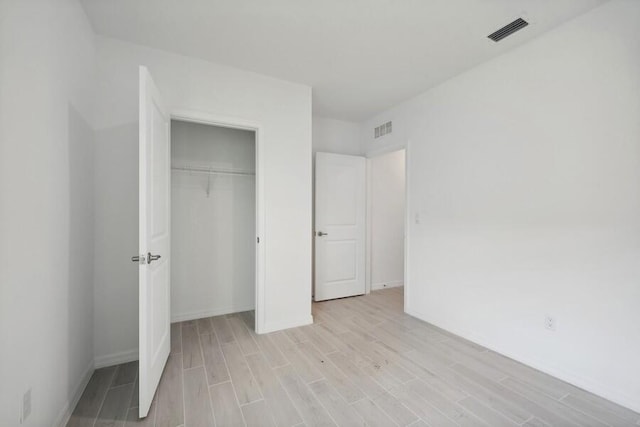 unfurnished bedroom featuring light wood finished floors, visible vents, and a closet