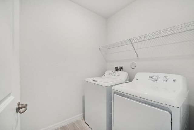 washroom with laundry area, separate washer and dryer, light wood-type flooring, and baseboards