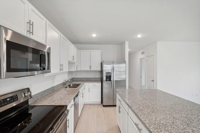 kitchen with appliances with stainless steel finishes, white cabinetry, a sink, and light stone counters