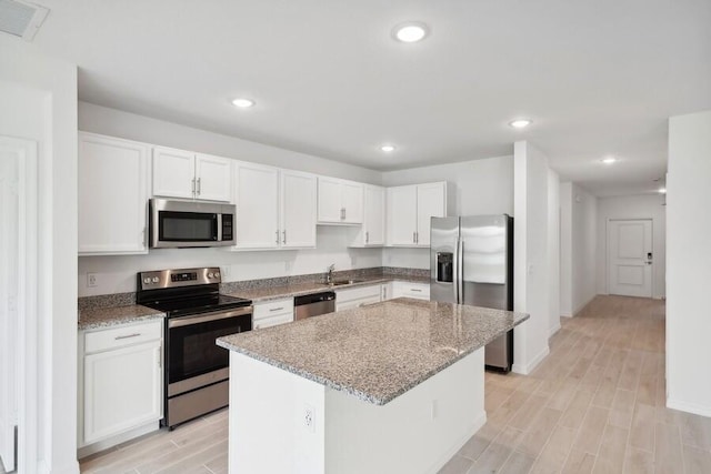 kitchen featuring appliances with stainless steel finishes, white cabinetry, a kitchen island, and light stone countertops