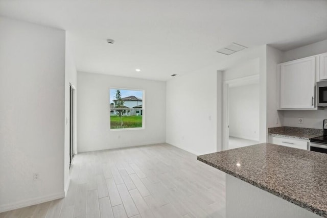 kitchen featuring white cabinetry, baseboards, light wood-style floors, dark stone counters, and stainless steel microwave