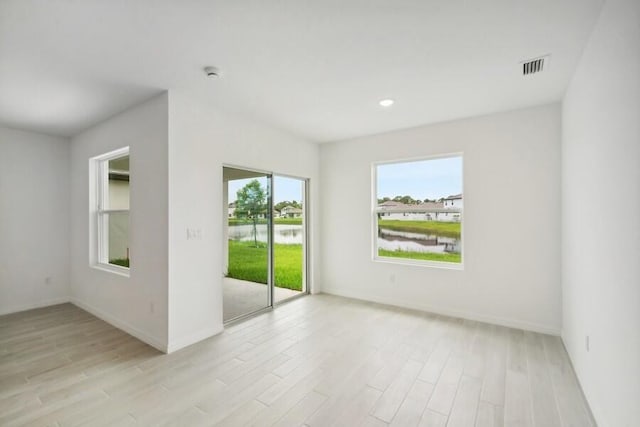 unfurnished room featuring visible vents, a water view, light wood-style flooring, and baseboards