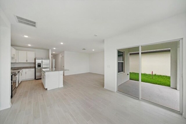 kitchen with stainless steel fridge, visible vents, white cabinets, a kitchen island, and open floor plan