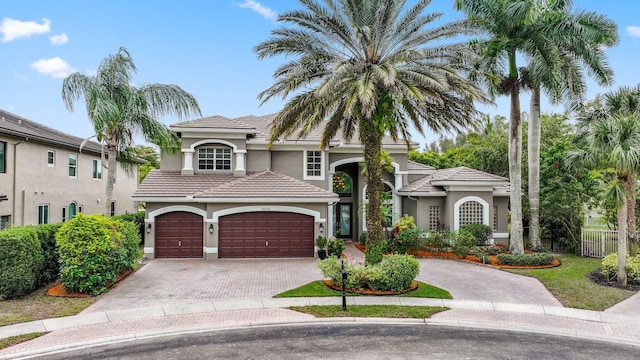 mediterranean / spanish house featuring a tiled roof, decorative driveway, an attached garage, and stucco siding