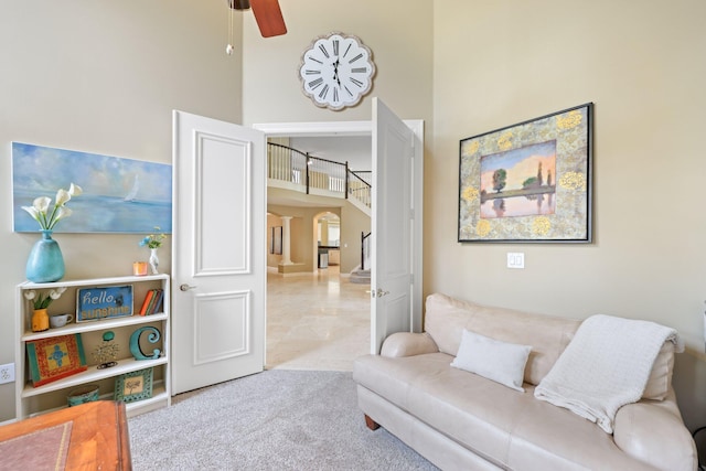 living area featuring arched walkways, a ceiling fan, light colored carpet, stairs, and a high ceiling