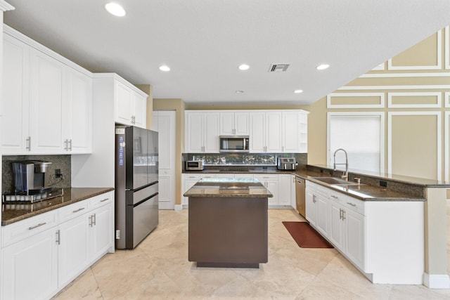 kitchen featuring a peninsula, a kitchen island, a sink, visible vents, and appliances with stainless steel finishes