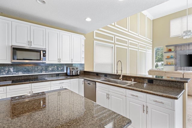 kitchen featuring tasteful backsplash, white cabinets, dark stone countertops, stainless steel appliances, and a sink