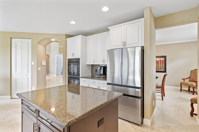 kitchen with arched walkways, white cabinetry, freestanding refrigerator, a center island, and dark stone counters