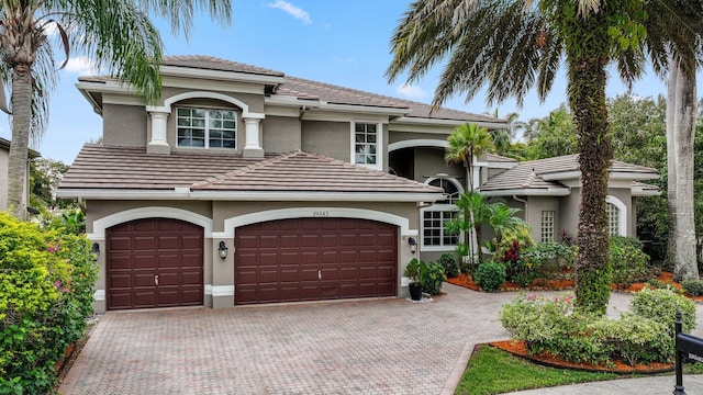 mediterranean / spanish-style house with decorative driveway, a tile roof, and stucco siding