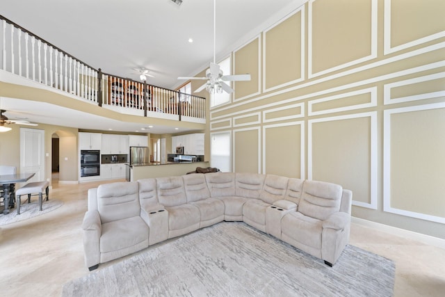 living room with arched walkways, a decorative wall, baseboards, and ceiling fan