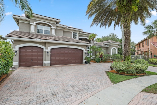 mediterranean / spanish-style house featuring a tiled roof, decorative driveway, and stucco siding