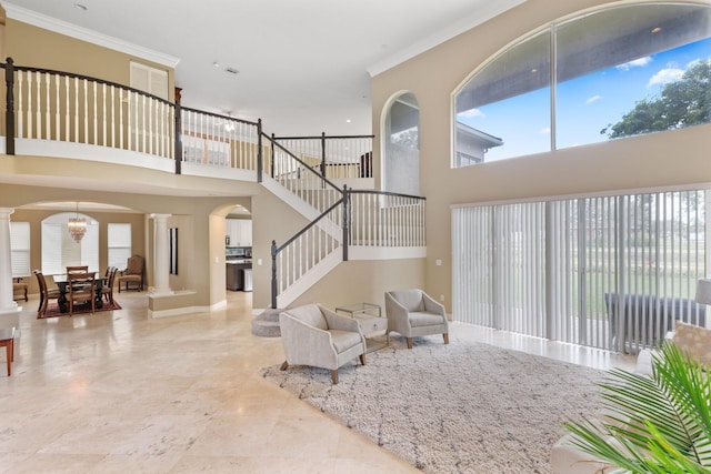 living area featuring arched walkways, crown molding, ornate columns, and stairs