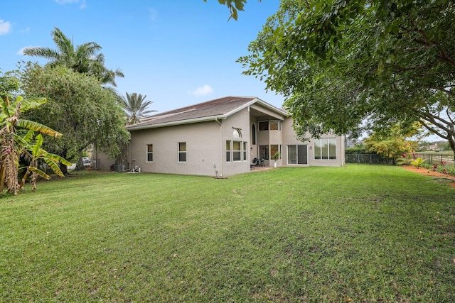 back of property featuring stucco siding, fence, and a lawn