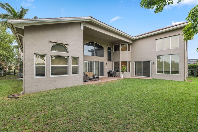 rear view of house with a patio area, fence, a lawn, and stucco siding