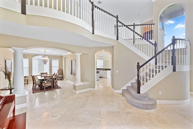 foyer with arched walkways, decorative columns, a towering ceiling, and baseboards