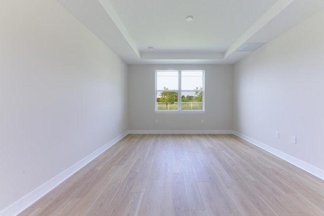 spare room featuring a tray ceiling, light wood-style flooring, and baseboards