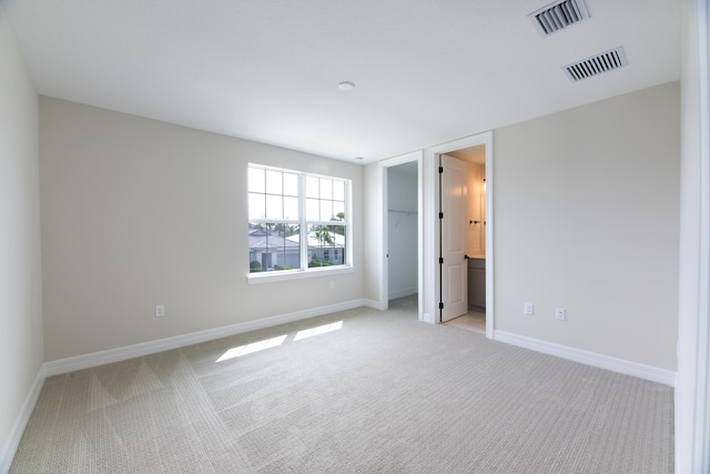 unfurnished bedroom featuring light carpet, a walk in closet, visible vents, and baseboards