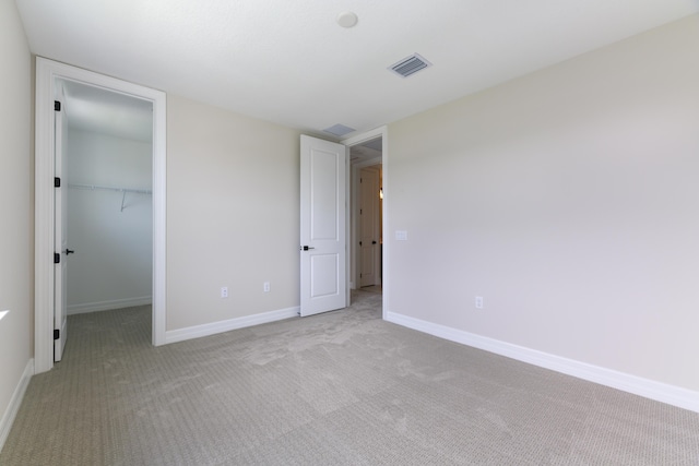 unfurnished bedroom with carpet floors, a walk in closet, visible vents, and baseboards